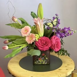 Pink roses and lilies in a square vase with a butterfly accent