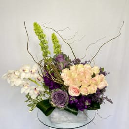 Arrangement of pale pink roses, white orchids, and purple flowers in a silver box
