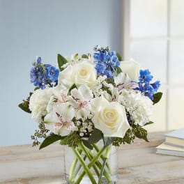 White roses and blue flowers arranged in a clear glass vase