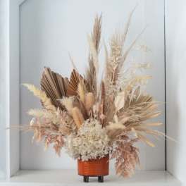 Tall dried arrangement of neutral pampas, palms, and hydrangea in a small orange pot