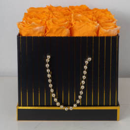 Orange roses arranged in a black and gold striped square box with a beaded handle