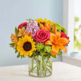 Colorful bouquet of sunflowers, roses, lilies, and mixed blooms in a glass vase