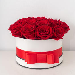 Round white hatbox filled with red roses and wrapped with a wide red ribbon and bow.