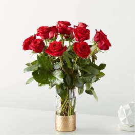 Red roses arranged in a clear glass vase with a gold-toned base