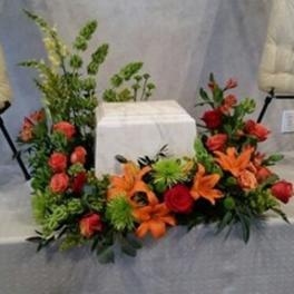 Floral arrangement with orange lilies and red roses around a white box