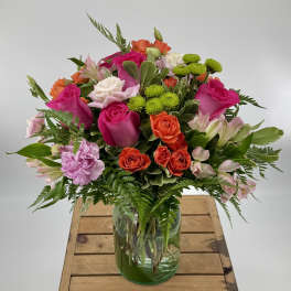 Mixed bouquet of pink, orange, white, and green flowers in a glass vase