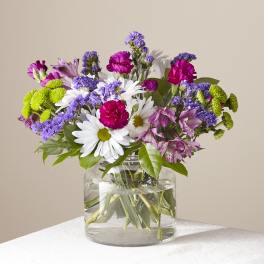 Mixed bouquet of daisies, carnations, and purple blooms in a glass vase