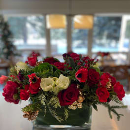 Red and white roses arranged in a low glass vase with holiday accents
