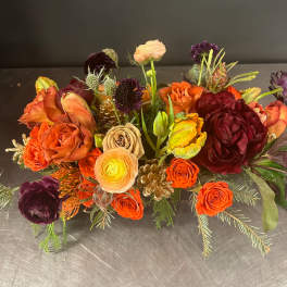 Low floral arrangement with orange, burgundy, and peach blooms