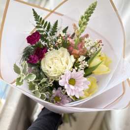 Hand-tied bouquet of mixed pastel flowers wrapped in white paper with a tan border