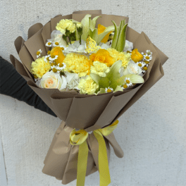 Hand-tied bouquet of yellow and white flowers wrapped in tan paper with a yellow ribbon