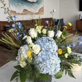 Blue and white floral arrangement with roses, hydrangeas, and yellow accents in a vase