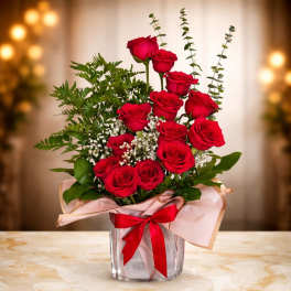Arrangement of red roses with white filler flowers in a square glass vase wrapped with a red bow