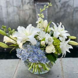 White lilies and blue hydrangeas in a clear glass vase