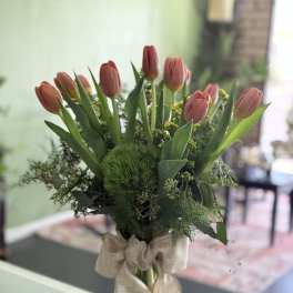 Pink tulips arranged in a clear glass vase with a burlap bow