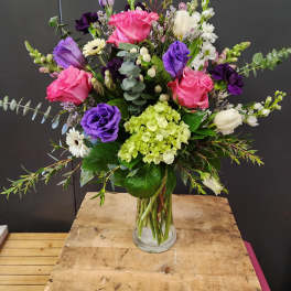 Mixed bouquet of pink, purple, white, and green flowers in a glass vase