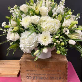 White floral arrangement in a white container with roses, lilies, and hydrangeas