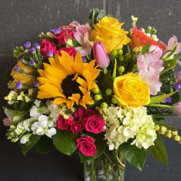 Colorful bouquet with sunflowers, roses, tulips, and alstroemeria in a glass vase