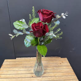 Two red roses in a clear glass vase with greenery