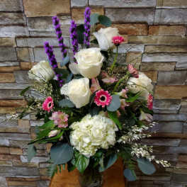 Tall bouquet of white roses, pink gerberas, and purple spikes in a glass vase