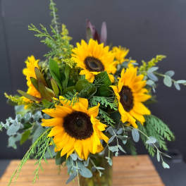 Sunflower bouquet in a glass vase with mixed greenery