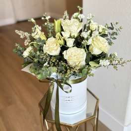 Cream roses and white blooms arranged in a white hat box with a ribbon