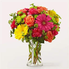 Mixed bouquet of pink, orange, and yellow flowers in a clear glass vase