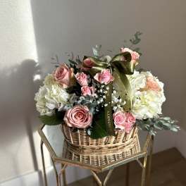 Pink roses and white hydrangeas in a wicker basket with a ribbon bow