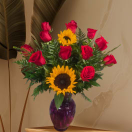 Red roses and sunflowers arranged in a purple glass vase