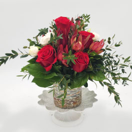 Red and white roses arranged in a glass vase with greenery