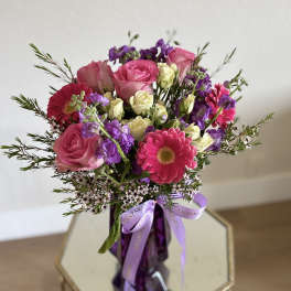 Pink roses and purple flowers in a purple vase with a ribbon