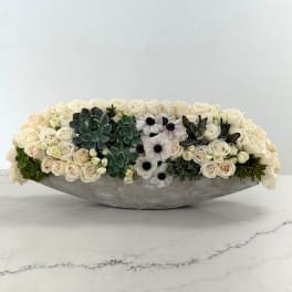 Low floral arrangement of cream roses, white anemones, and succulents in a gray container
