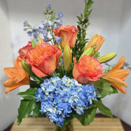 Orange roses and lilies with blue hydrangeas in a vase