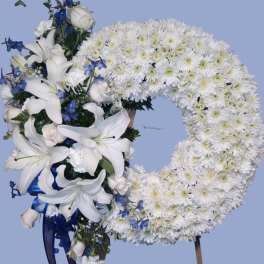 White floral wreath with lilies and blue accents on a stand
