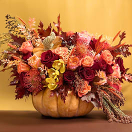 Autumn floral arrangement in a pumpkin container with roses and orchids