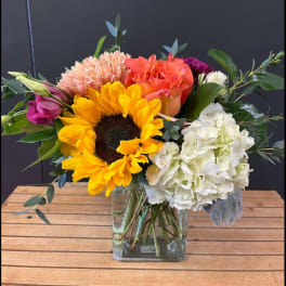 Mixed bouquet with sunflower, hydrangea, and roses in a glass vase