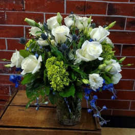 White roses and blue flowers arranged in a clear glass vase.