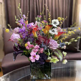 Mixed bouquet in a square glass vase with pink, purple, white, and orange blooms