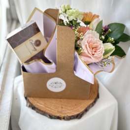 Gift caddy with pastel mixed flowers and a box of chocolates on a wood slice base.