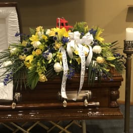 Large funeral casket spray with yellow, white, and blue flowers