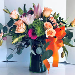 Mixed bouquet of peach roses, lilies, and green chrysanthemums in a dark vase