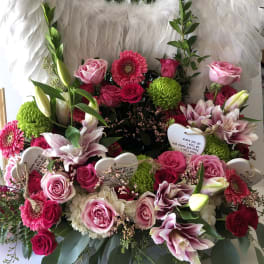 Pink and red floral arrangement with white feather wings and heart tags
