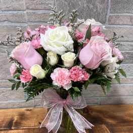 Pink and white roses with pink carnations in a clear glass vase tied with a pink ribbon bow