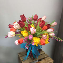 Colorful tulip bouquet in a glass vase with a blue ribbon