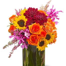 Bright mixed bouquet in a glass vase with sunflowers, roses, and purple blooms
