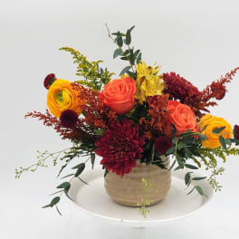 Mixed bouquet in a beige vase with orange, yellow, and burgundy flowers