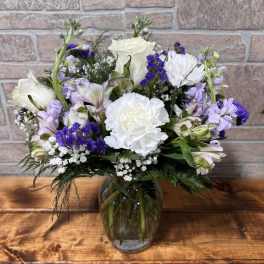Mixed bouquet of white and purple flowers in a clear glass vase on a wooden surface