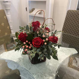 Red roses arranged in a dark vase with pink berries and greenery