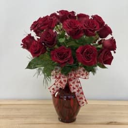 Red roses arranged in a glass vase with a heart-patterned ribbon