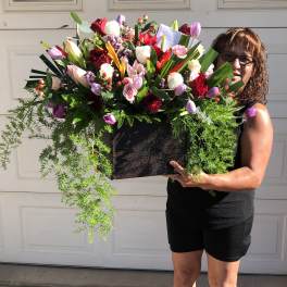 Large mixed flower arrangement in a black container held by a woman
